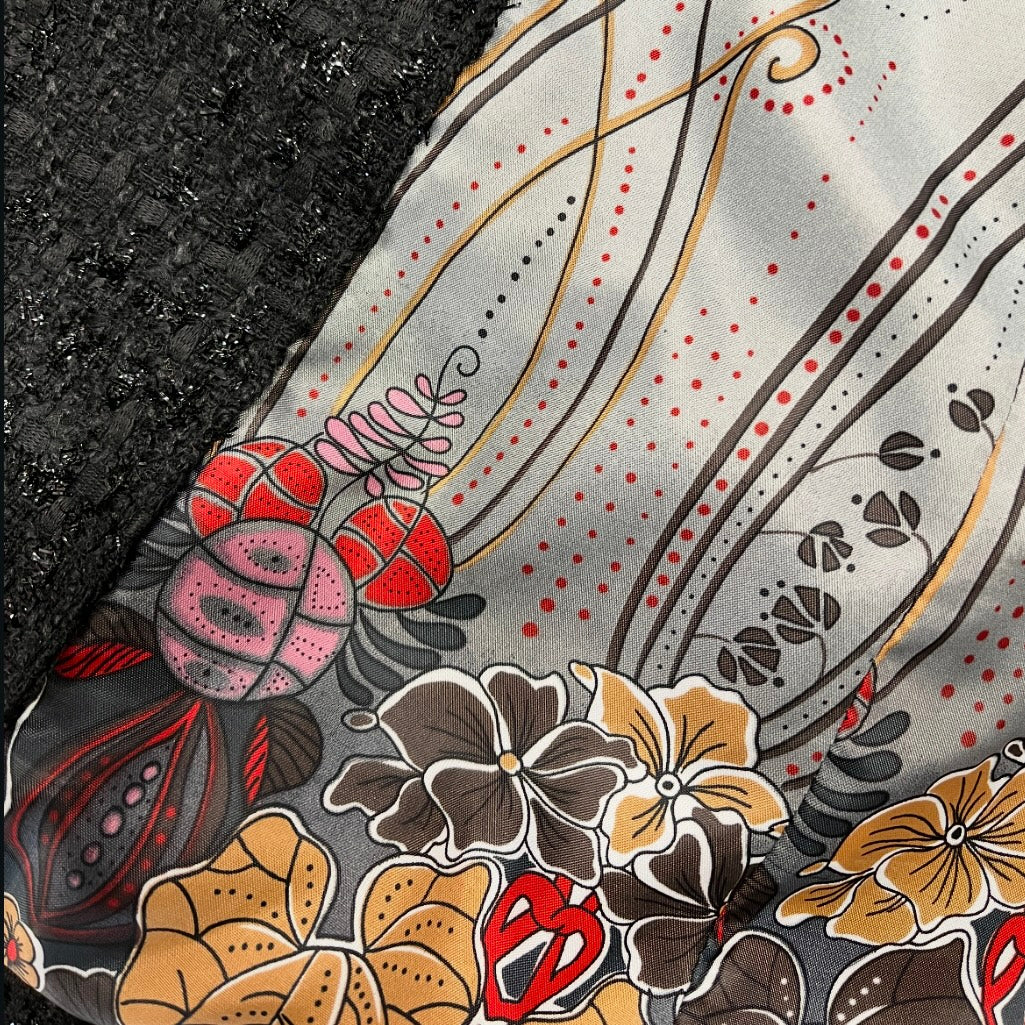 Close-up of a fabric with intricate floral and paisley patterns in red, brown, and beige on a black background.