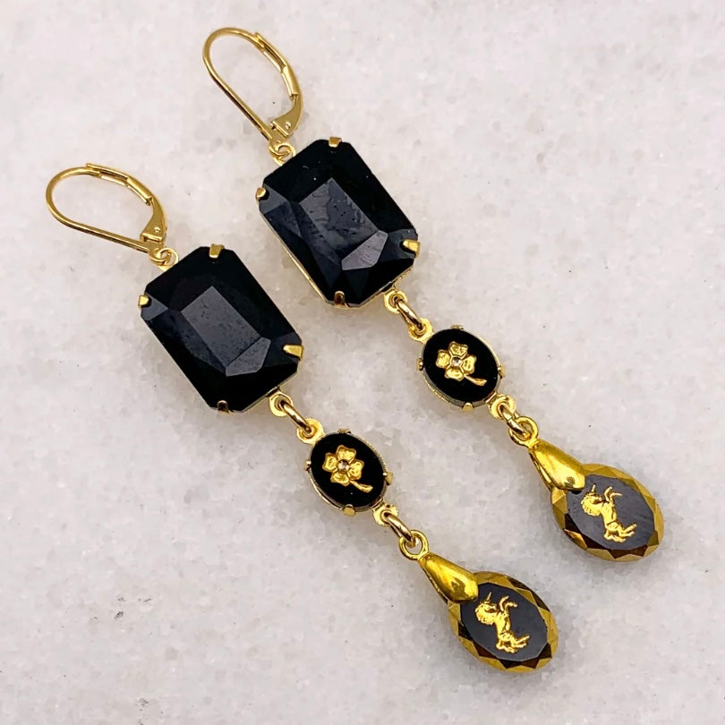 Gold and black earrings on a textured white background