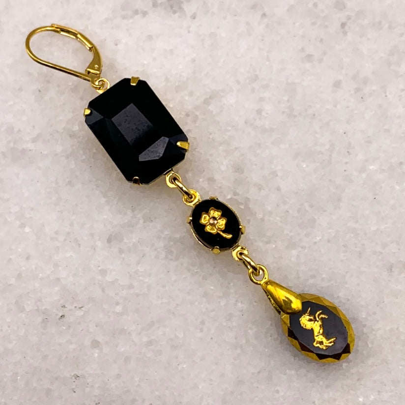 Gold and black earring with a textured gray background