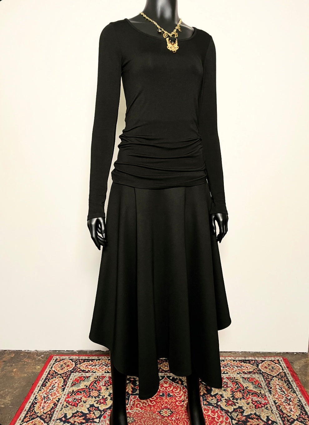 Black dress on a mannequin with a gold necklace against a white background